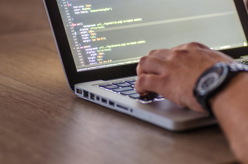 Close-up of a white Puma baseball cap positioned in front of a laptop with a black keyboard and a red backlit, on a desk. The laptop screen displays blurred lines of code, suggesting a tech or work-re